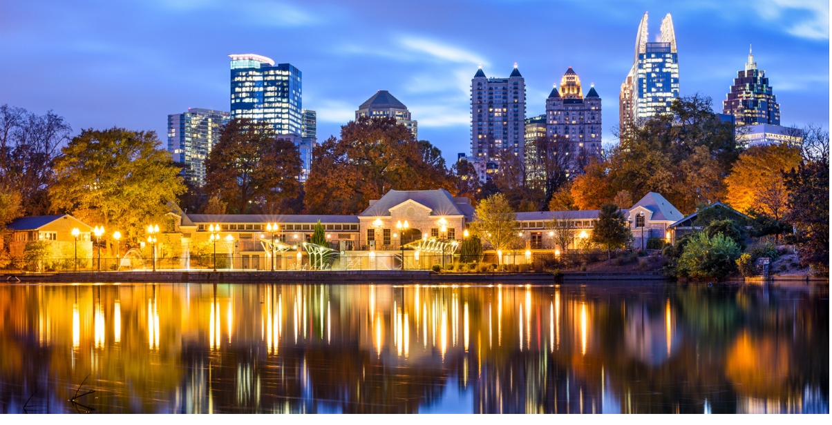 Atlanta skyline at dusk reflected in Lake Clara Meer at Piedmont Park, with autumn trees lining the water